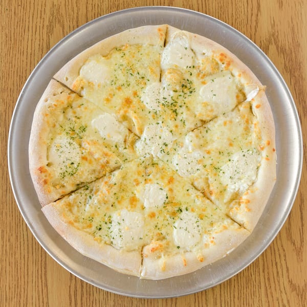 A white pizza with mozzarella, ricotta, and parsley on a metal tray on a wooden table.
