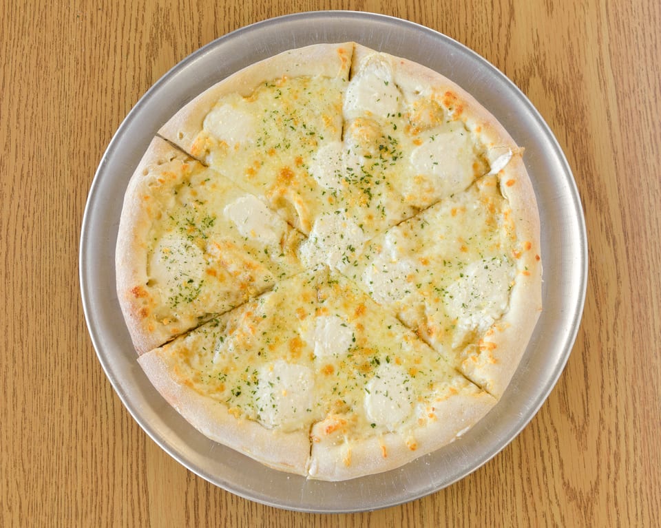 A white pizza with mozzarella, ricotta, and parsley on a metal tray on a wooden table.