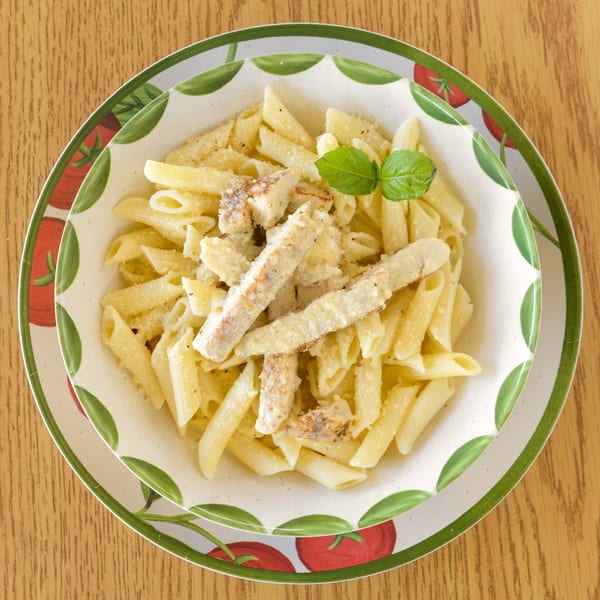 Penne pasta with chicken and parmesan cheese, garnished with basil, in a decorative bowl.
