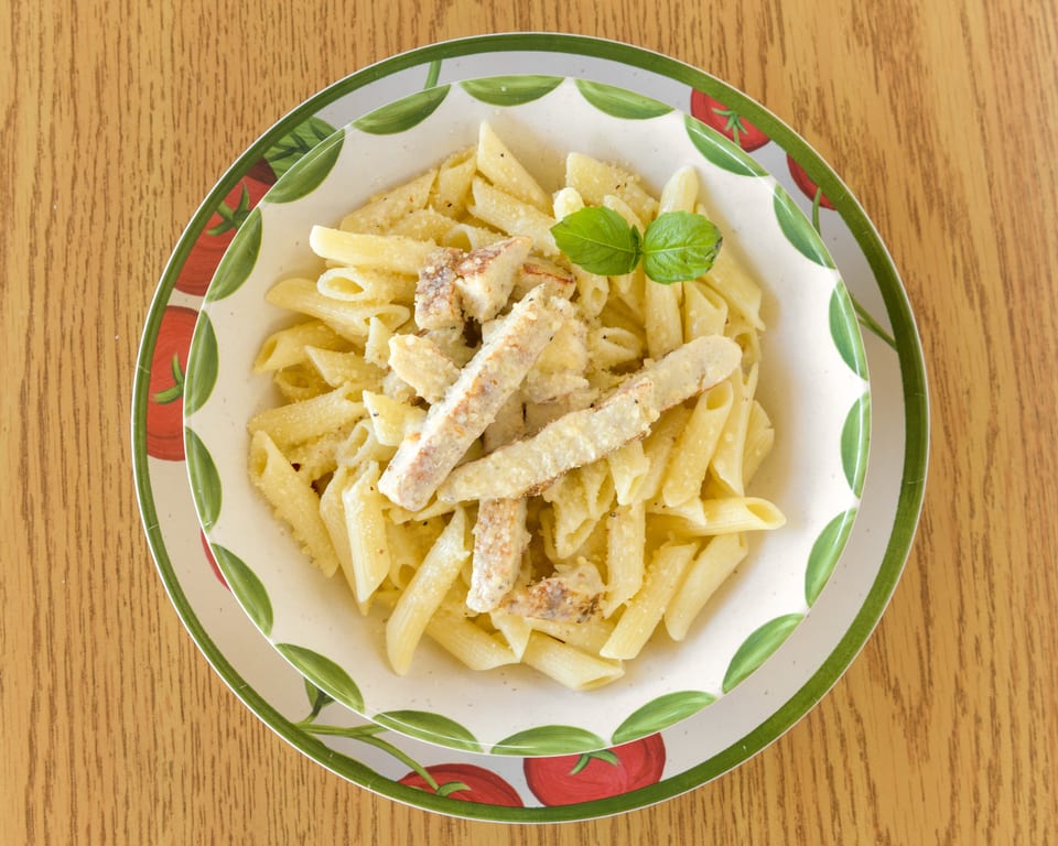 Penne pasta with chicken and parmesan cheese, garnished with basil, in a decorative bowl.