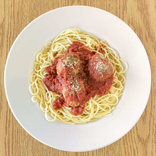 Spaghetti with three large meatballs, marinara sauce, and parmesan cheese on a white plate.