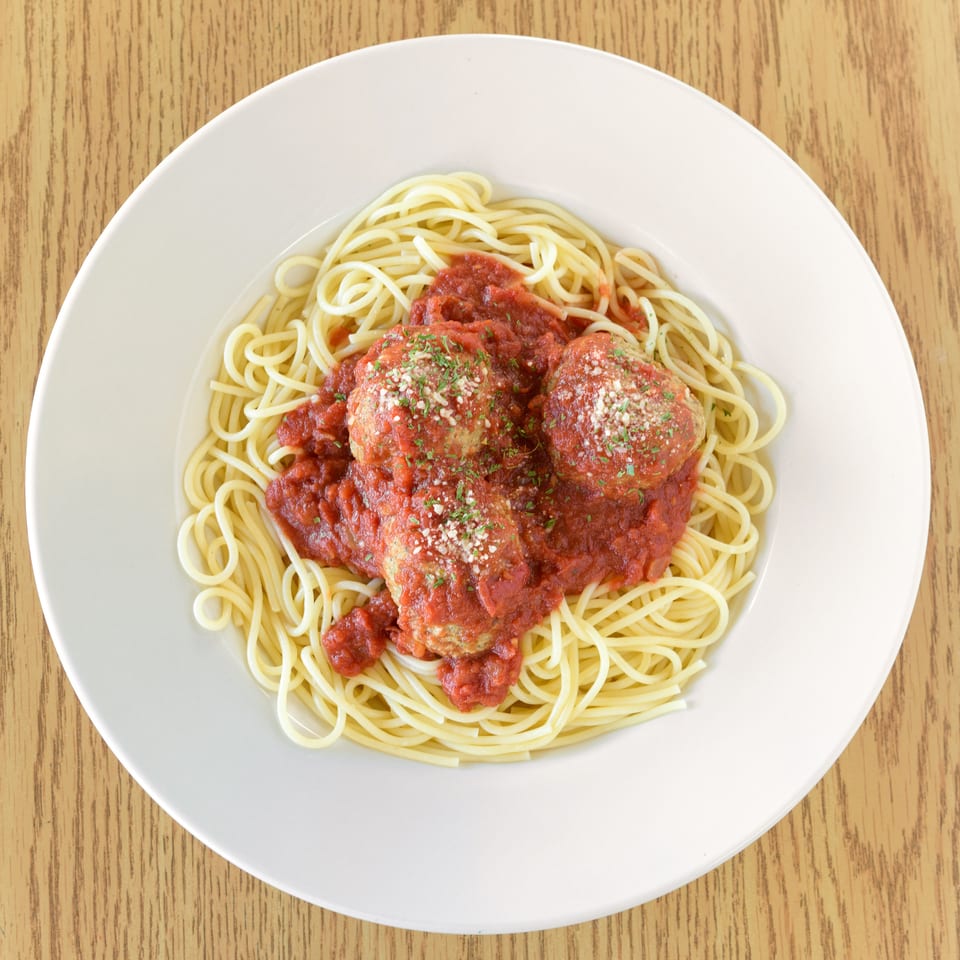 Spaghetti with three large meatballs, marinara sauce, and parmesan cheese on a white plate.