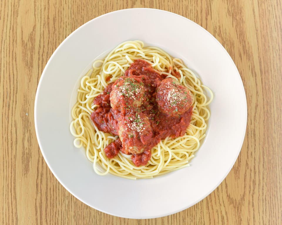 Spaghetti with three large meatballs, marinara sauce, and parmesan cheese on a white plate.