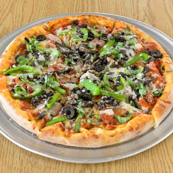 Whole pizza with green peppers, black olives, mushrooms, and cheese on a metal pan.