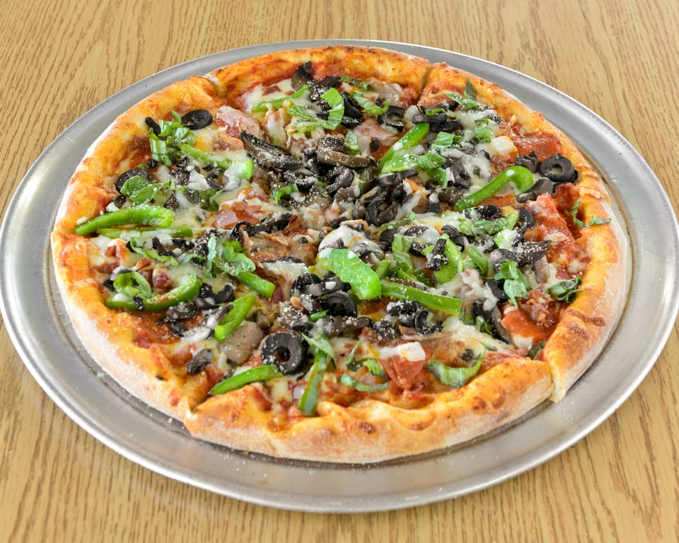 Whole pizza with green peppers, black olives, mushrooms, and cheese on a metal pan.